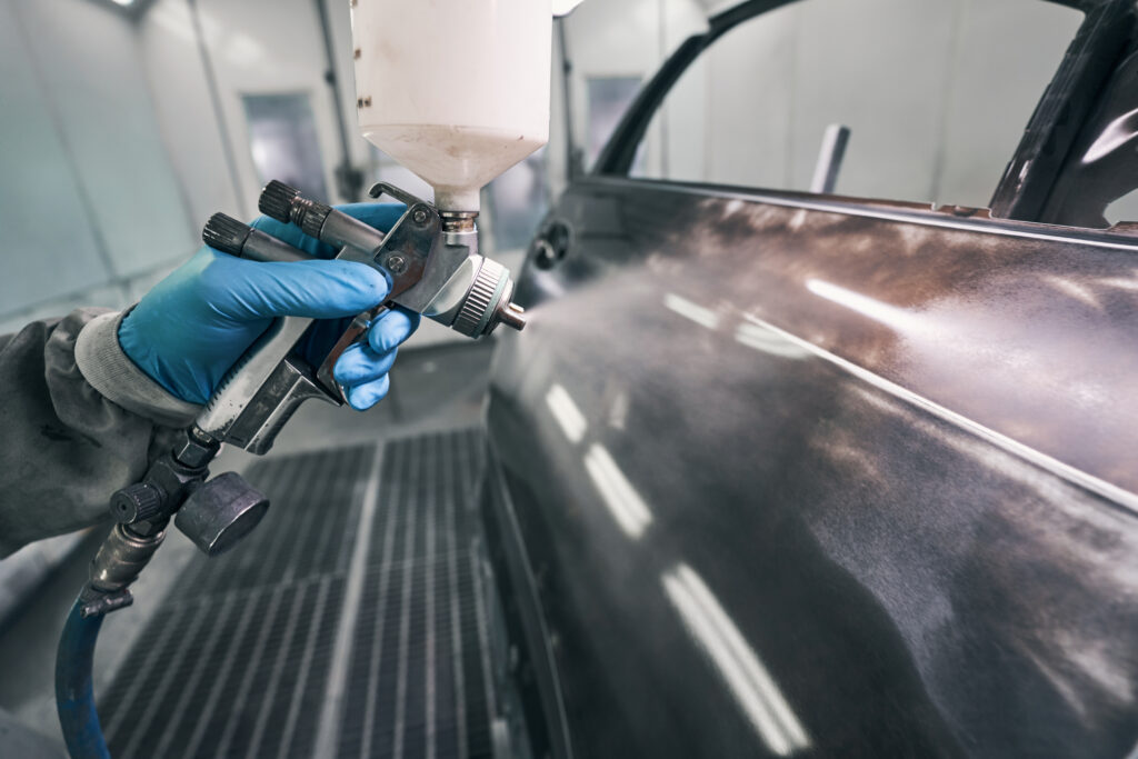 Automobile technician painting auto with spraying gun